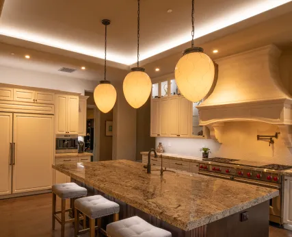 A modern kitchen at night with warm pendant lighting, illustrating Control4 architectural lighting scenes
